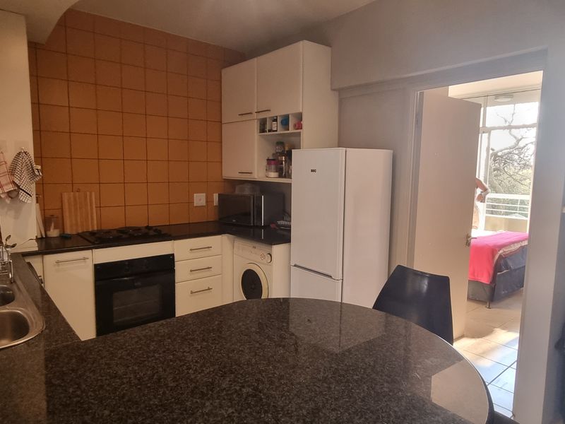 A functional kitchen featuring granite countertops, built-in cabinetry, a gas hob, and an integrated oven, with a view into the adjacent bedroom.