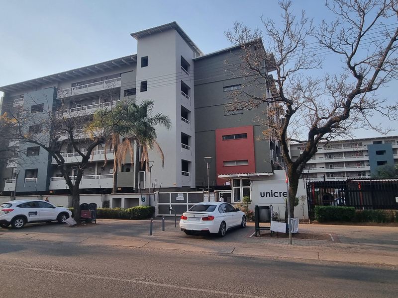 Front exterior view of a multi-story apartment complex featuring modern facade finishes, balconies, and secure gated access from the street.