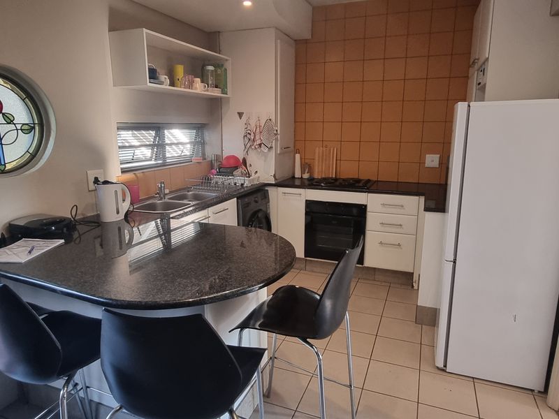 Compact kitchen featuring a granite breakfast bar, built-in oven, gas hob, tiled splashback, and a unique stained glass porthole window.