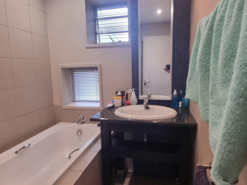 A functional bathroom featuring a bathtub, vanity basin with dark cabinetry, tiled walls, and natural light from two windows.