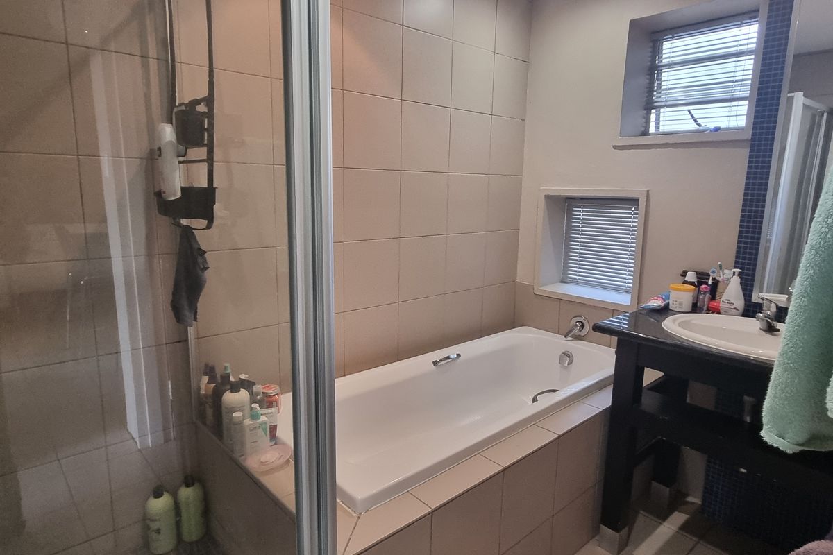 A functional bathroom featuring a built-in bathtub, separate shower enclosure, and a vanity basin with tiled finishes throughout.
