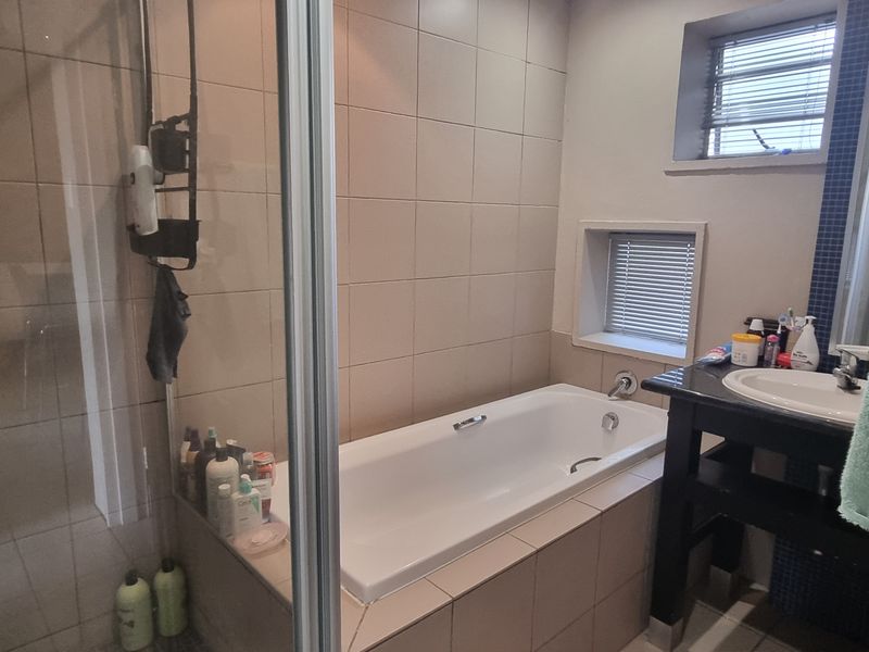 A functional bathroom featuring a built-in bathtub, separate shower enclosure, and a vanity basin with tiled finishes throughout.