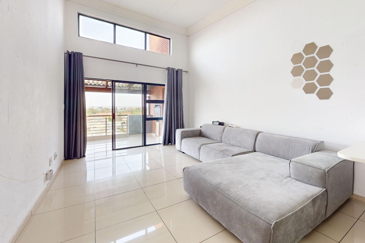 Spacious living room featuring high ceilings, large tiled flooring, and a sliding glass door leading to an outdoor balcony area.