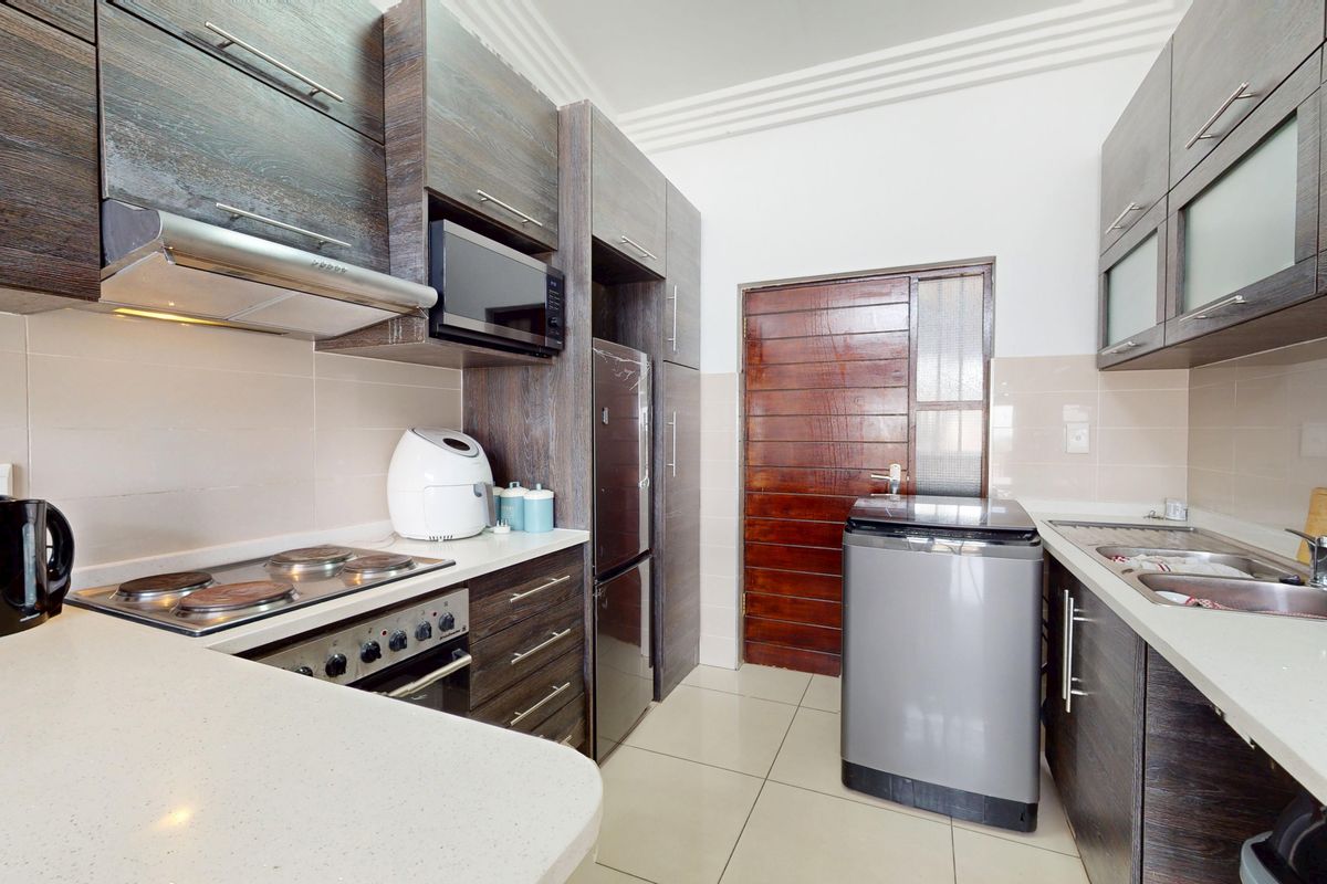 Modern kitchen featuring dark wood cabinetry, stone countertops, integrated appliances, and a tiled backsplash, offering a functional and contemporary cooking space.