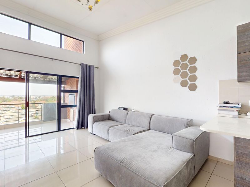 Open-plan living area featuring high ceilings, tiled floors, and large sliding doors leading to a balcony, with an adjacent kitchen area.