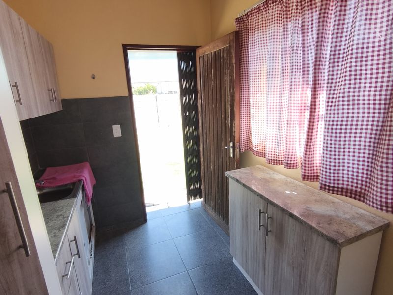 A functional scullery area featuring built-in cabinetry, stone-look countertops, tiled flooring, and direct access to the exterior.