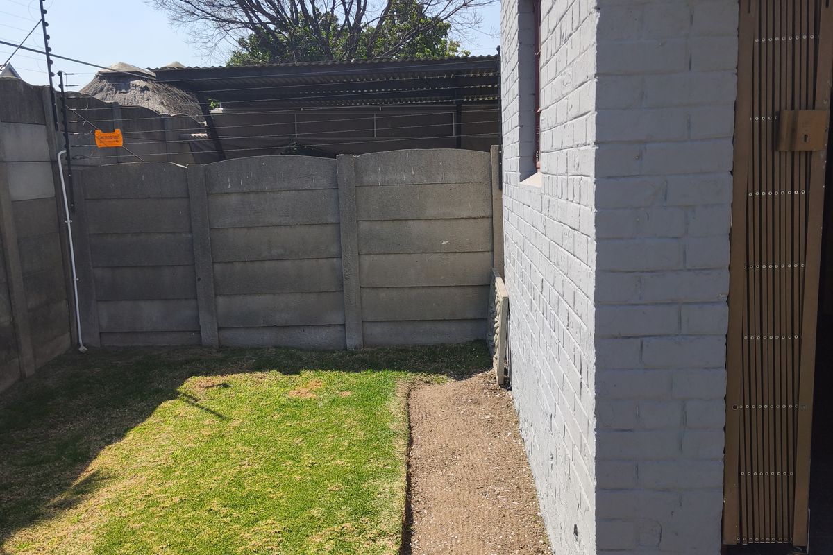 A rear exterior view of the townhouse featuring a small lawn, perimeter precast concrete walling with electric fencing, and a painted brick facade.