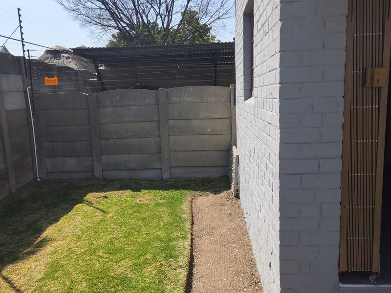 A rear exterior view of the townhouse featuring a small lawn, perimeter precast concrete walling with electric fencing, and a painted brick facade.