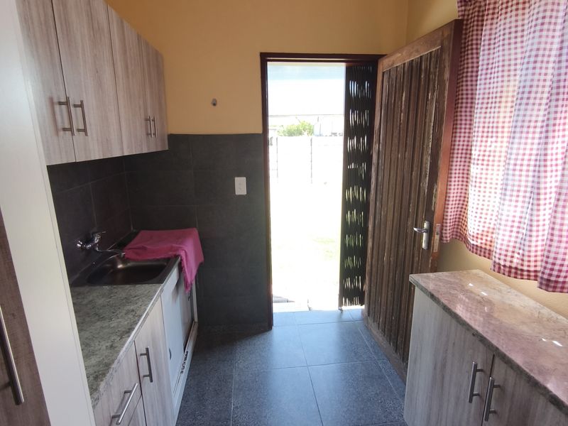 A functional scullery featuring built-in cabinetry, granite countertops, a stainless steel sink, and direct access to the exterior.