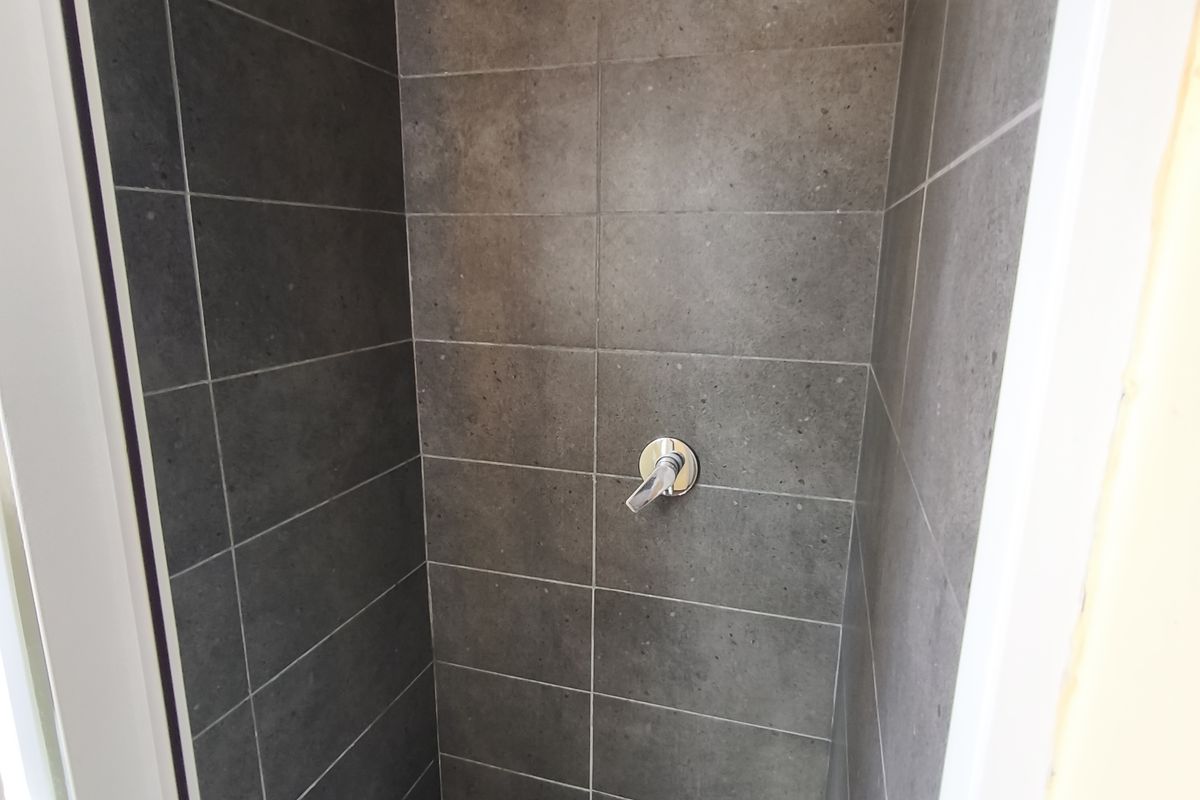 A modern walk-in shower enclosure featuring dark grey wall tiles, a contrasting checkered floor, and a contemporary square rainfall shower head.