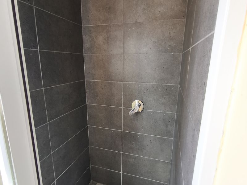 A modern walk-in shower enclosure featuring dark grey wall tiles, a contrasting checkered floor, and a contemporary square rainfall shower head.