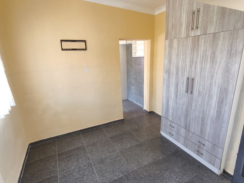 An empty bedroom featuring dark tiled flooring, a modern wood-grain built-in wardrobe, and yellow painted walls with coving.