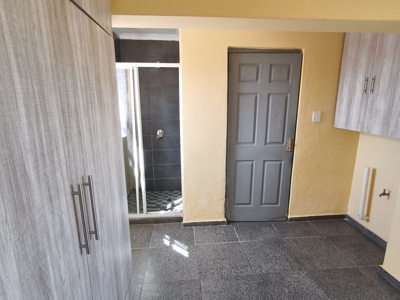 A functional laundry area featuring built-in cabinetry, tiled flooring, and an adjacent shower enclosure, offering practical utility space within the townhouse.