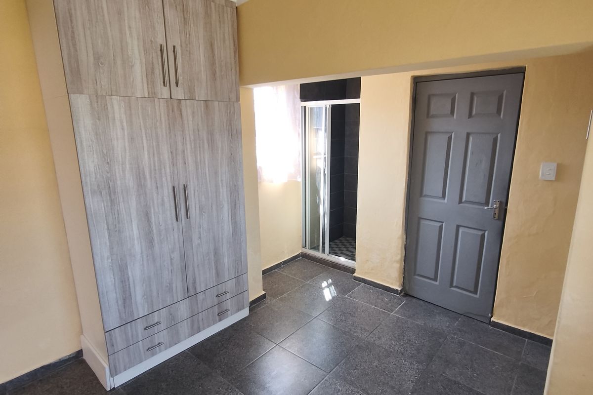 A bedroom featuring dark tiled flooring, a built-in wardrobe, and an en-suite shower cubicle.