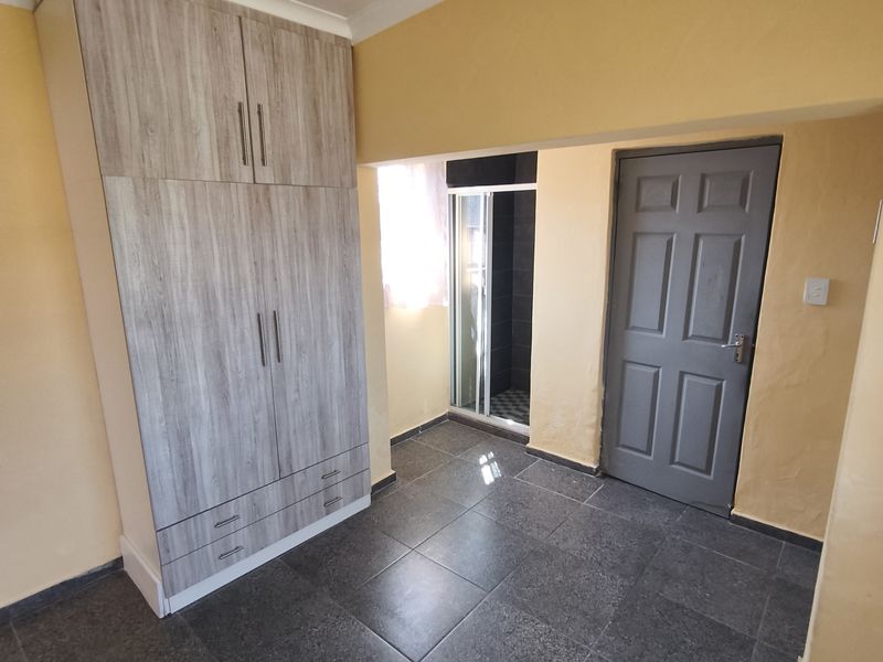 A bedroom featuring dark tiled flooring, a built-in wardrobe, and an en-suite shower cubicle.