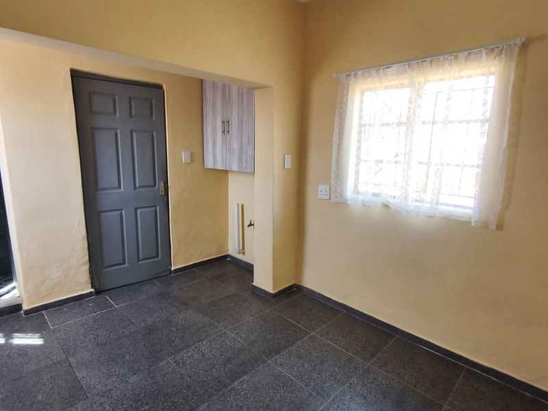 An empty kitchen area featuring dark tiled flooring, built-in cabinetry, and a window with security bars, offering a functional space ready for updates.