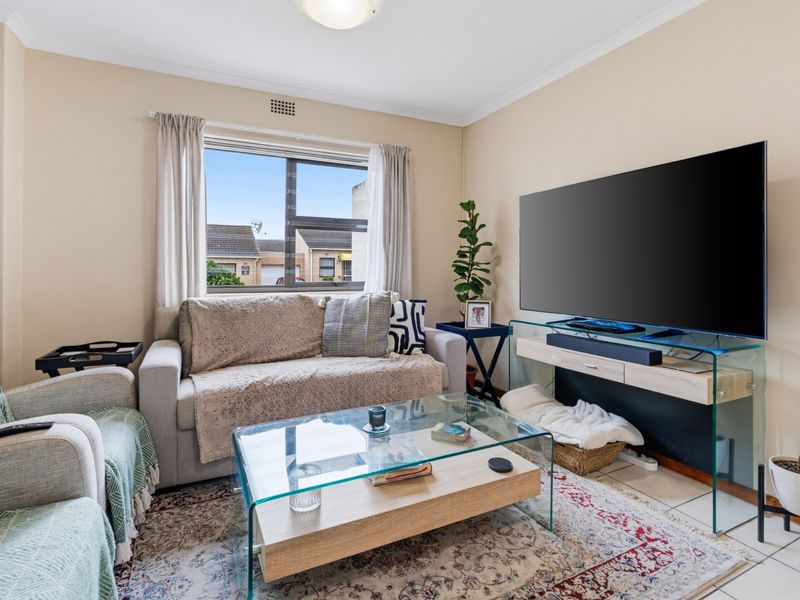 A comfortable living room featuring tiled flooring, neutral wall tones, and a large window providing natural light.