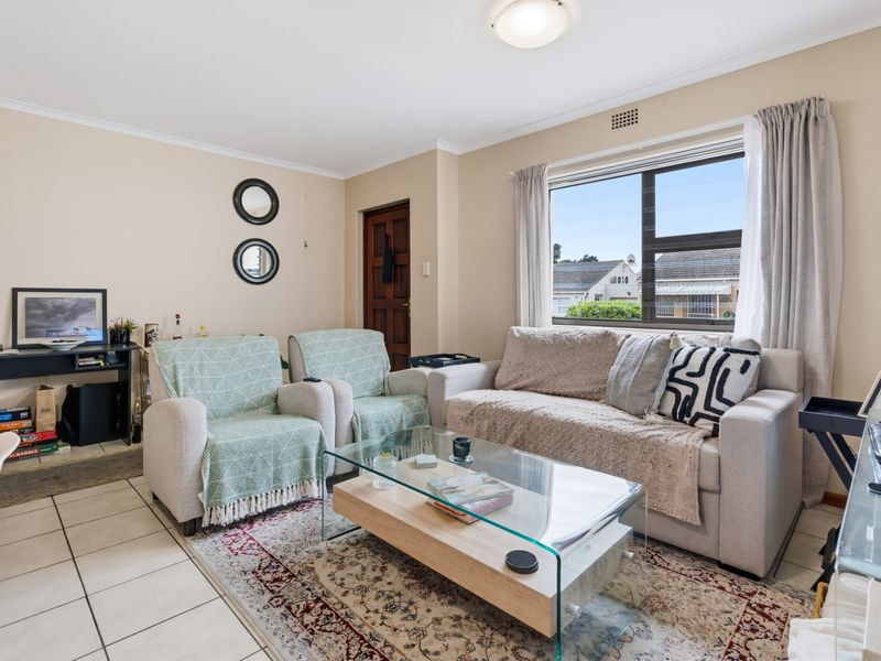 A comfortable living room featuring tiled flooring, neutral wall tones, and a large window providing natural light.