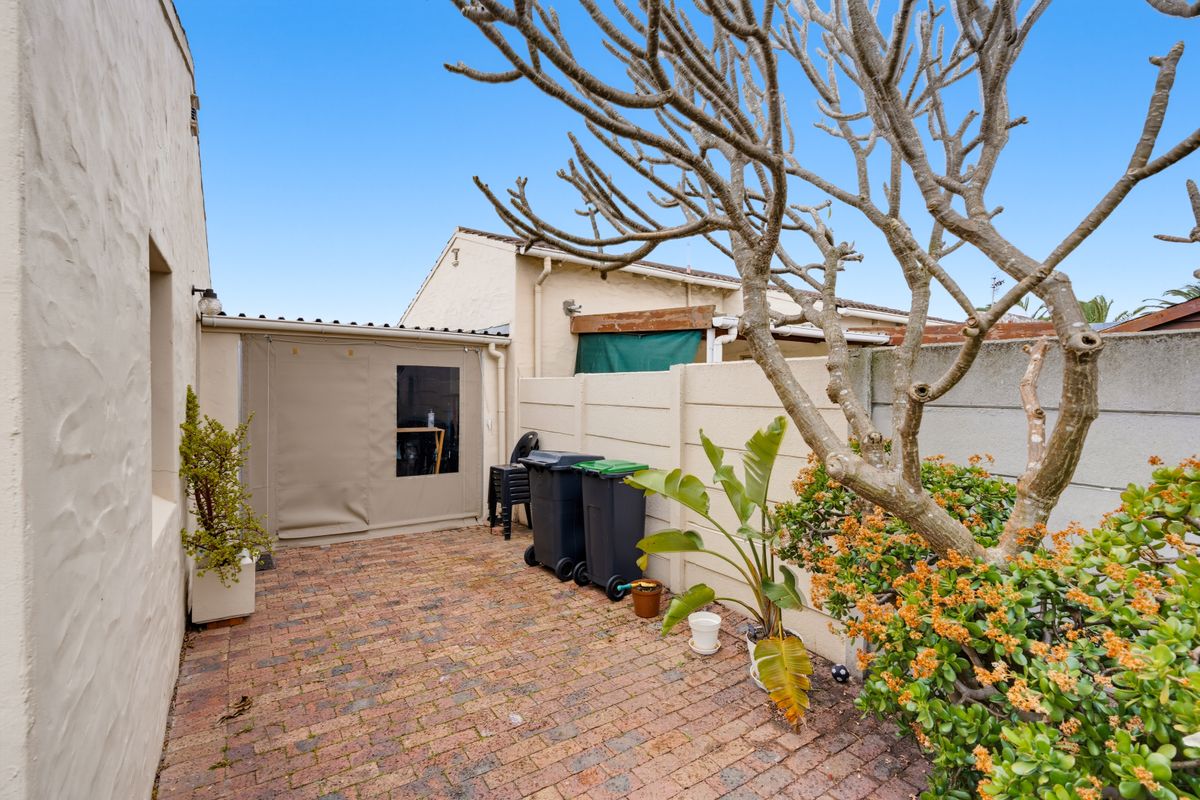 A private rear courtyard featuring brick paving, a precast concrete boundary wall, and a covered patio area with a canvas enclosure.