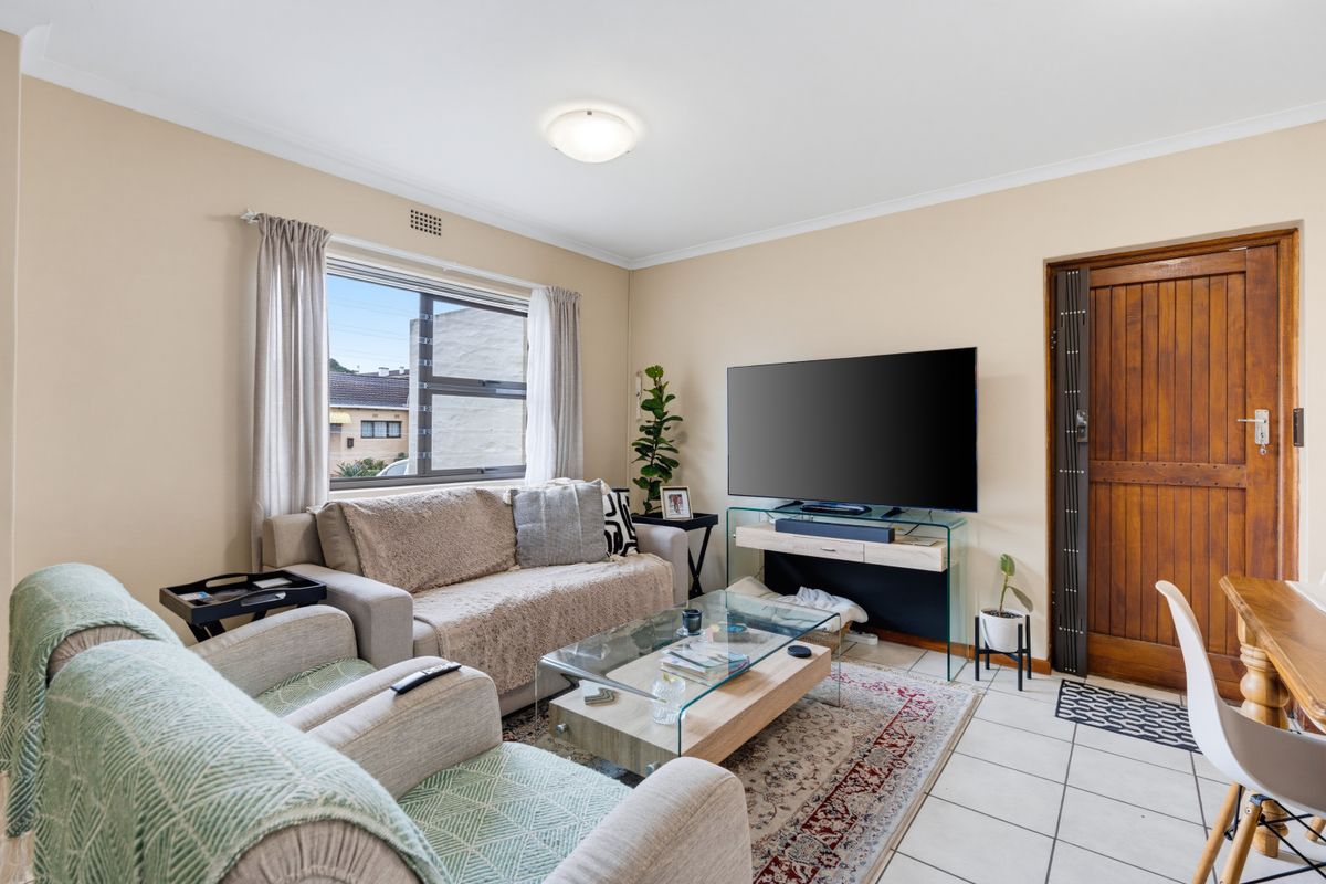 A comfortable living room featuring tiled flooring, neutral wall tones, and a large window providing natural light.