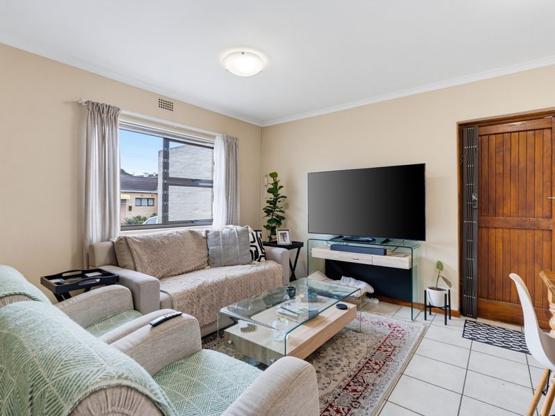 A comfortable living room featuring tiled flooring, neutral wall tones, and a large window providing natural light.