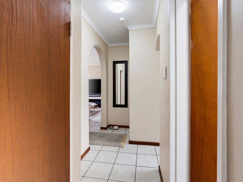A clean, tiled hallway featuring an arched entryway leading into the main living area, finished with neutral walls and coving.