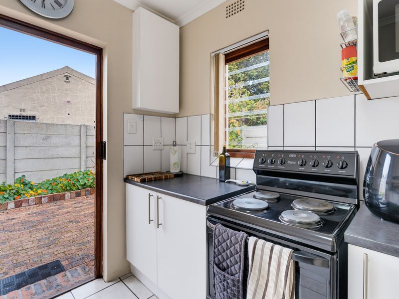 A functional kitchen featuring white cabinetry, dark countertops, a tiled backsplash, and a freestanding electric stove, with direct access to an outdoor patio area.