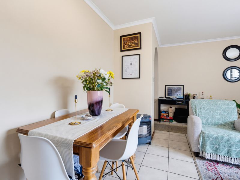 A living and dining area featuring tiled flooring, neutral wall tones, and a classic archway leading to an adjacent space.