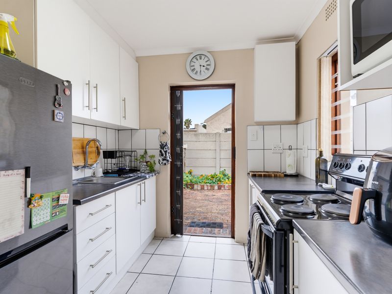 Compact galley-style kitchen featuring white cabinetry, dark countertops, tiled backsplash, and direct access to the rear outdoor area.