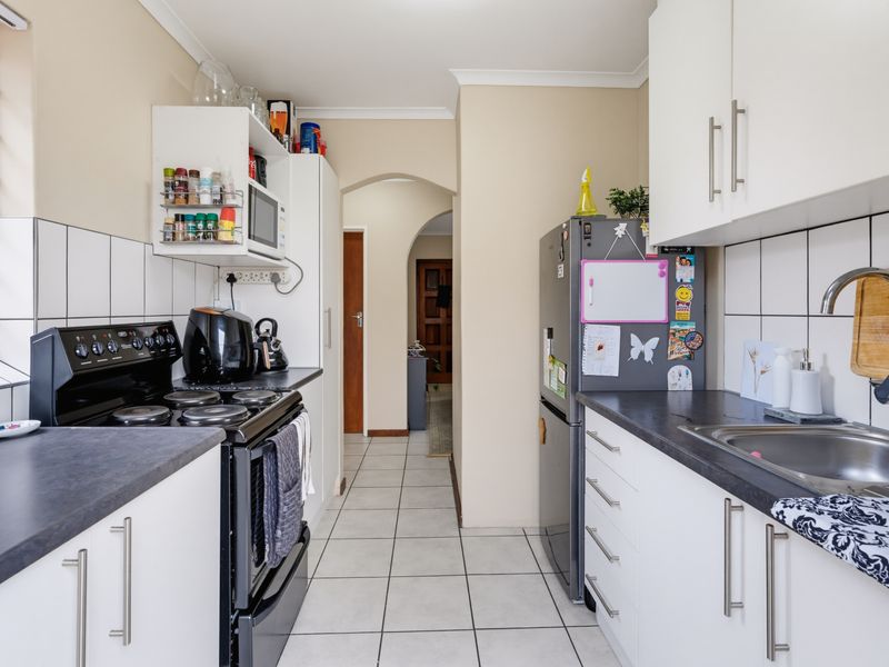 A functional galley-style kitchen featuring white cabinetry, dark laminate countertops, tiled splashbacks, and a freestanding stove, leading through an archway to the hallway.