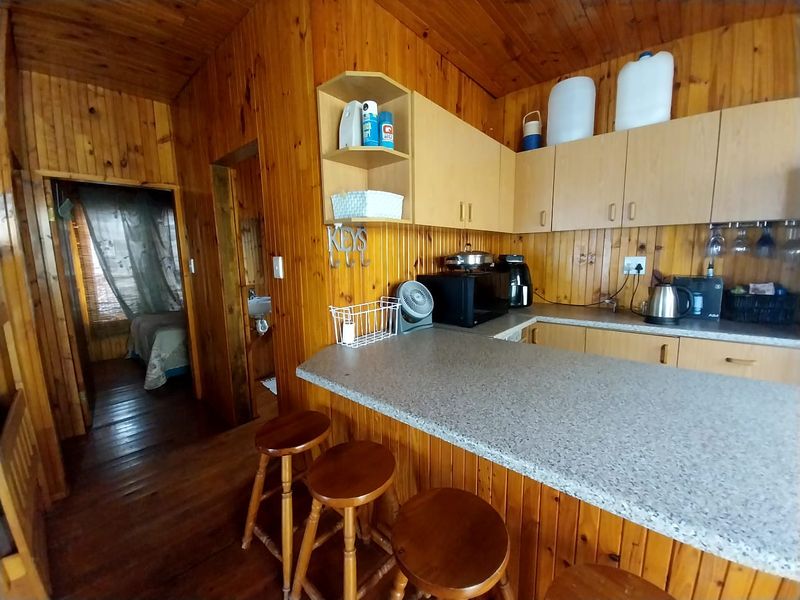 A dated kitchen featuring timber wall paneling, laminate countertops, and a breakfast bar, with an adjacent view into a bedroom and bathroom area.