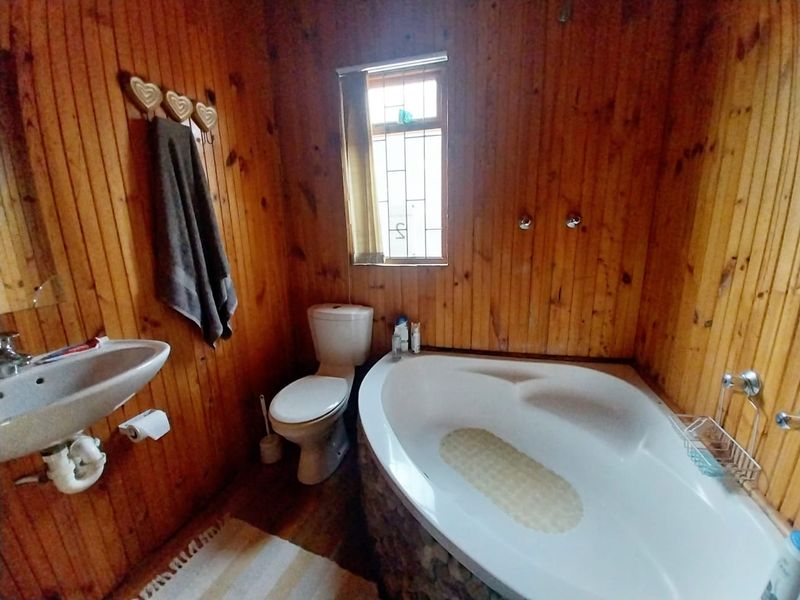 A bathroom featuring timber wall paneling, a corner bathtub, a pedestal basin, and a toilet with security bars on the window.