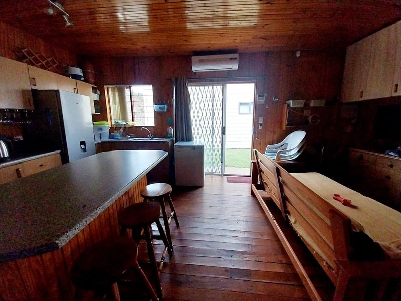 Open-plan living and kitchen area featuring timber wall paneling, wood flooring, and direct access to the rear garden through a sliding glass door.
