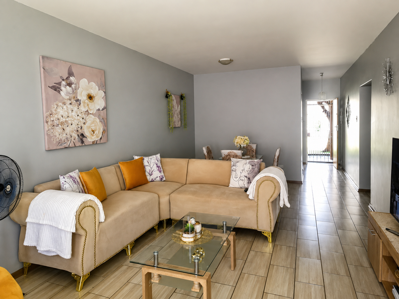 A well-maintained living room featuring neutral grey walls and light-toned tiled flooring, leading towards an entrance area with natural light.