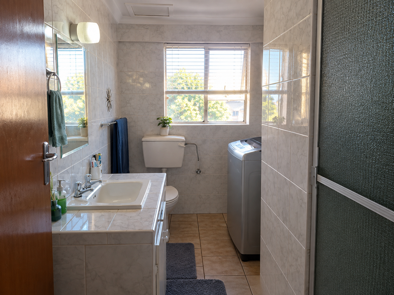 A functional bathroom featuring tiled walls and flooring, a vanity basin, a toilet, and a shower enclosure with natural light from the window.