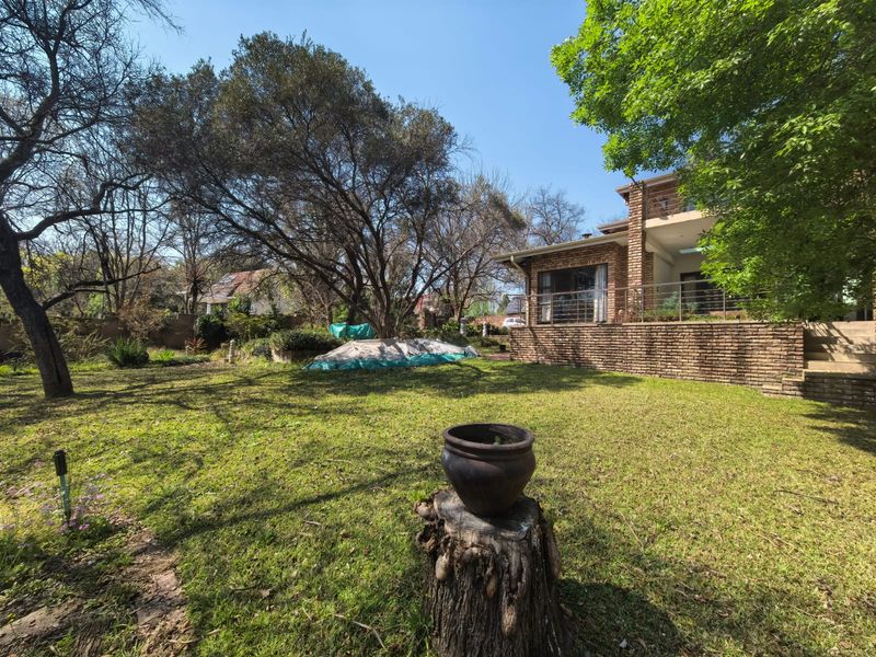 Spacious rear garden featuring a mature tree, lawn area, and a raised brick patio with metal railings attached to the townhouse.