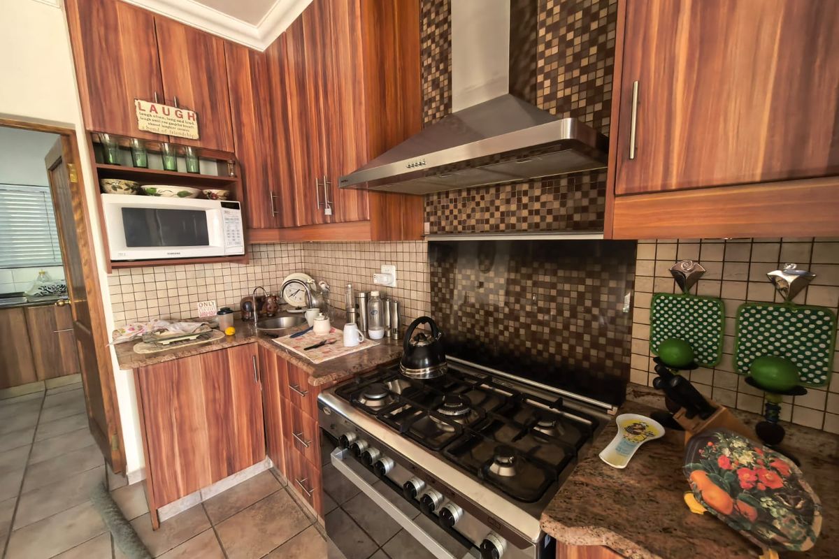 A functional kitchen featuring wood-grain cabinetry, granite countertops, a gas stove with an extractor fan, and a tiled backsplash.