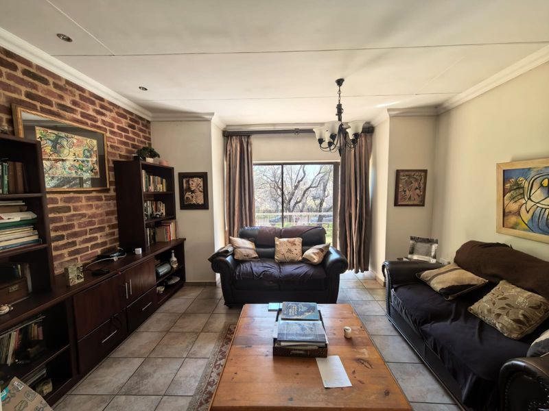 A comfortable living room featuring an exposed brick accent wall, tiled flooring, and a sliding glass door providing natural light and garden access.