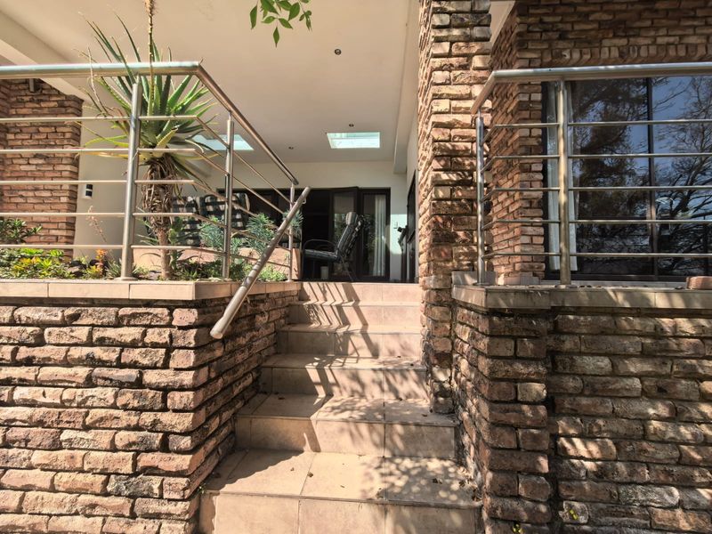 A covered patio area featuring exposed brick columns, stainless steel railings, tiled steps, and integrated skylights leading to the main living area.