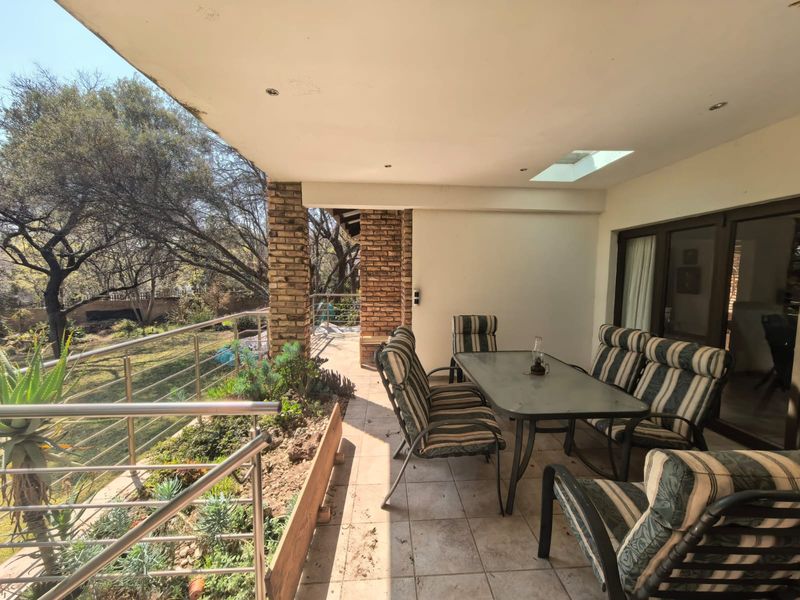 Covered patio featuring exposed brick pillars, stainless steel balustrade, tiled flooring, and a skylight, overlooking the garden area.