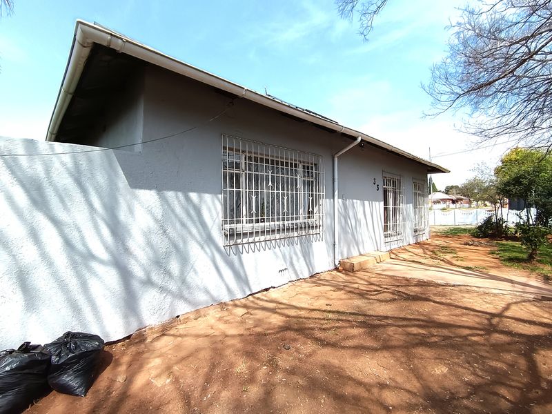 Front elevation of a single-story house featuring plastered walls, security bars on windows, and basic guttering, set on an unlandscaped plot.