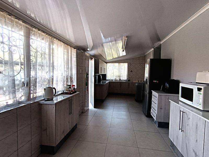 A functional kitchen featuring extensive built-in cabinetry, tiled flooring, and tiled splashbacks, with natural light provided by large windows fitted with security bars.