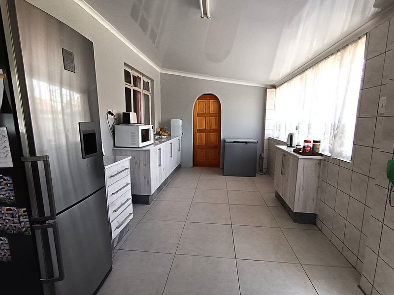 A functional scullery or utility area featuring tiled flooring, built-in cabinetry, and an arched wooden door leading to the main living space.