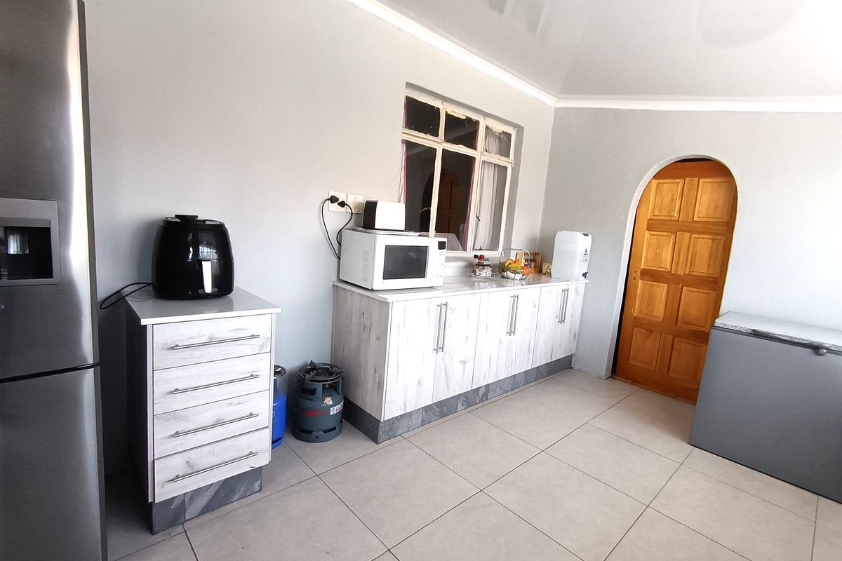 A functional kitchen area featuring light-toned built-in cabinetry, tiled flooring, and a distinctive arched wooden door leading to an adjacent space.