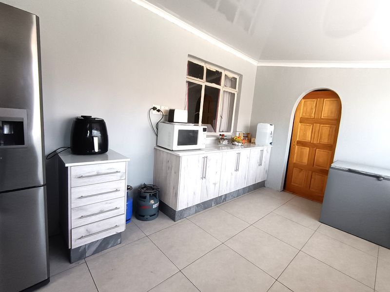 A functional kitchen area featuring light-toned built-in cabinetry, tiled flooring, and a distinctive arched wooden door leading to an adjacent space.