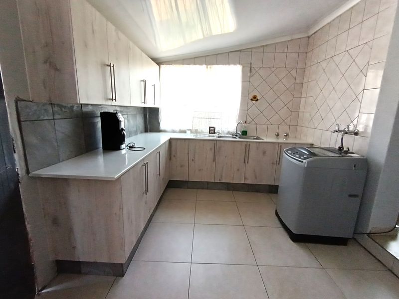 A functional scullery area featuring light wood-look cabinetry, tiled splashbacks, and dedicated plumbing connections for laundry appliances.