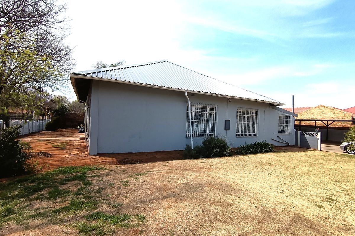 Rear view of the house featuring a corrugated metal roof, security bars on windows, and a surrounding yard area.