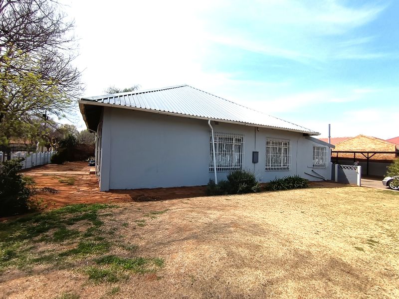 Rear view of the house featuring a corrugated metal roof, security bars on windows, and a surrounding yard area.