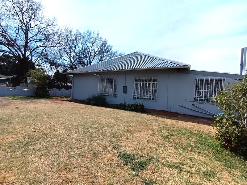 Rear view of the property featuring a corrugated metal roof, security bars on windows, and a spacious garden area.