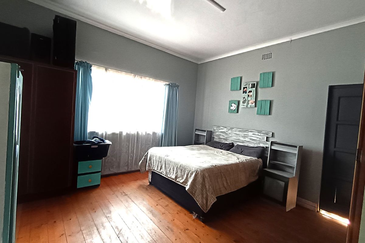 A spacious bedroom featuring warm timber flooring, neutral wall tones, and a built-in headboard, offering a comfortable and functional living space.